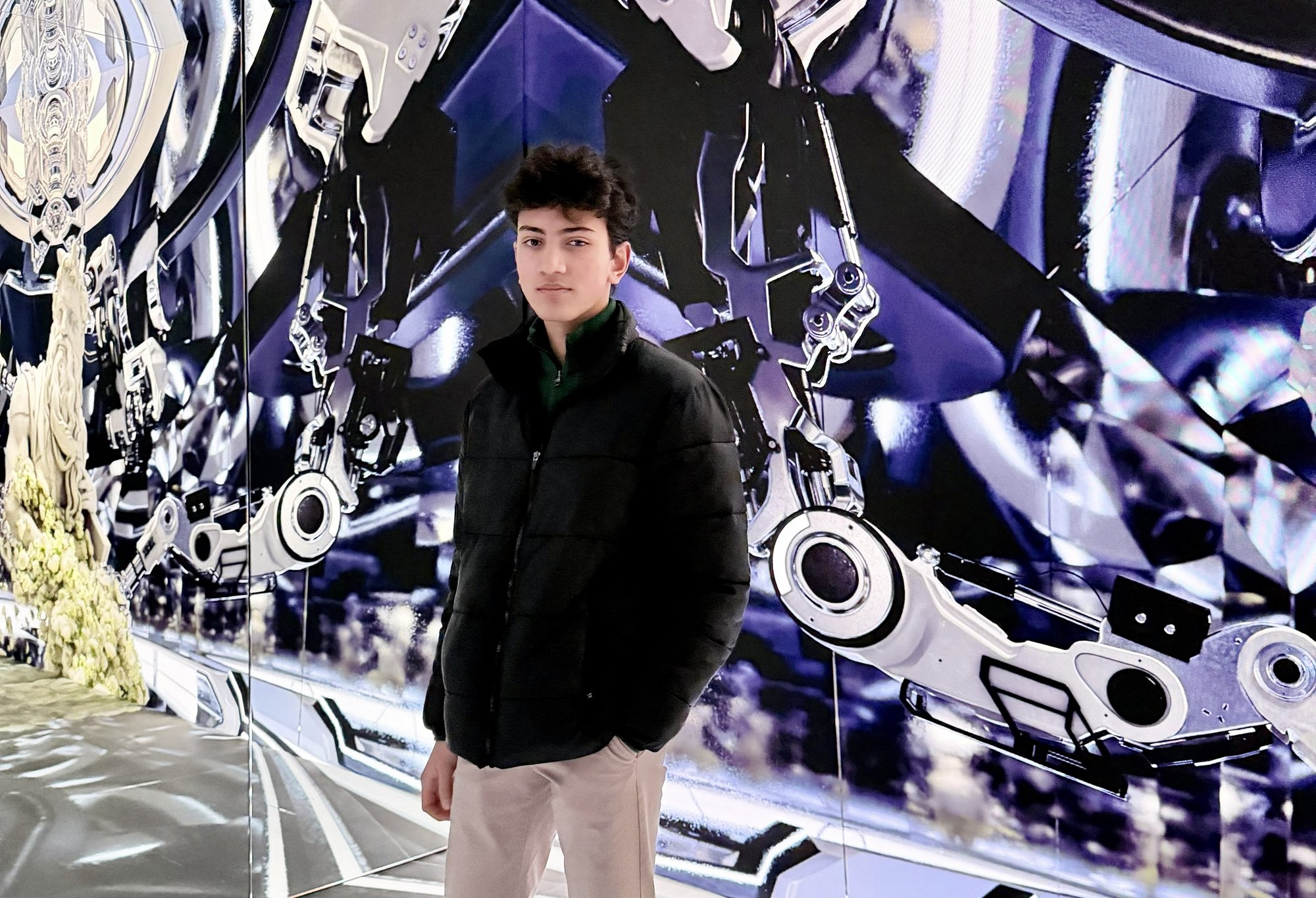 Standing in front of a mirrored robotic-arm mural at an immersive art installation